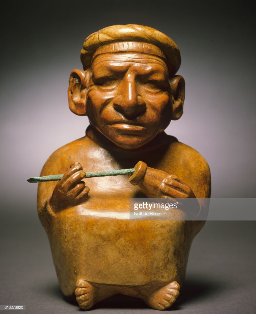 Moche ceramic vessel of a person chewing coca leaves and holding a gourd of lime.